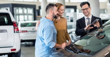 Cars salesman displaying information on a tablet to a couple inside a showroom.