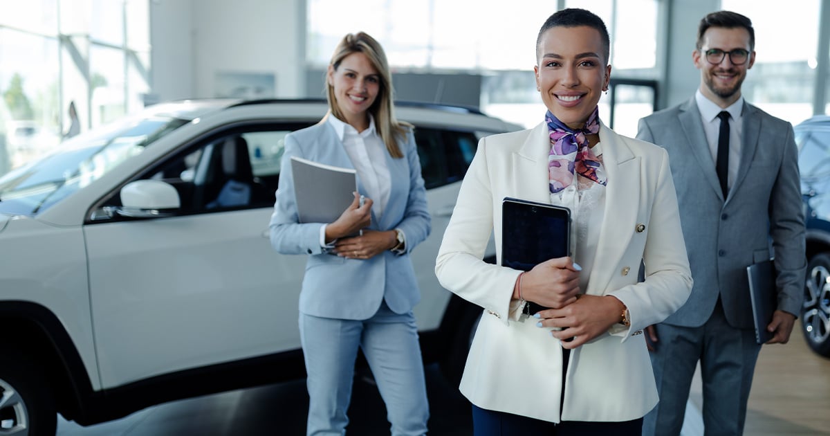 A sales team posing in front of a new car inside a dealership.