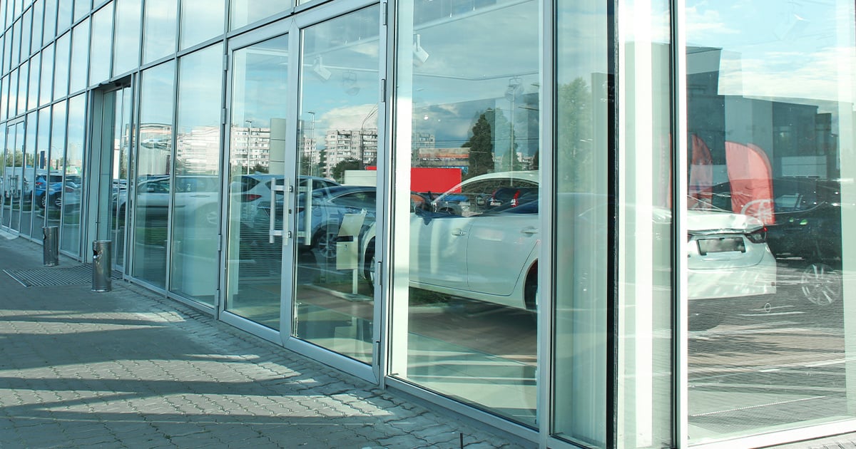 Exterior view of a modern glass-walled car dealership building with cars inside.