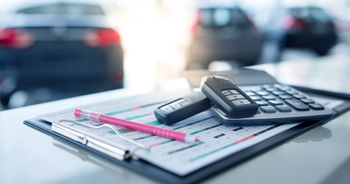 Image of car showroom with calculator and two new remote keys placed on a counter in the foreground.